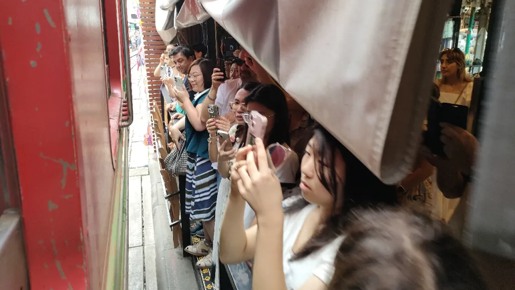 メークロン市場でお店の隙間に立って通過する列車を撮影する観光客