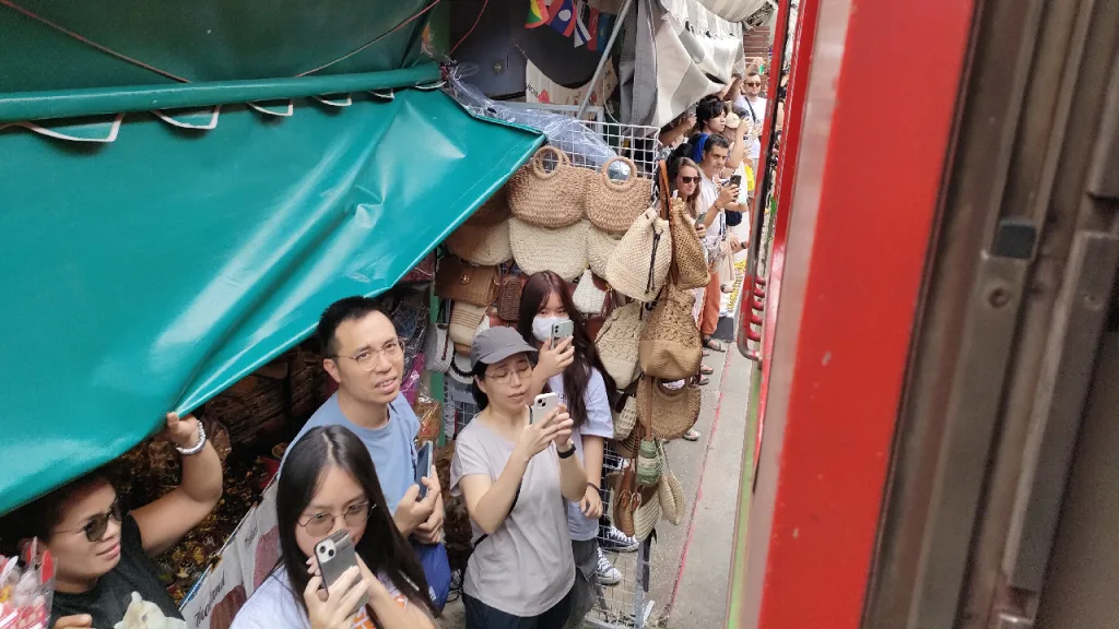メークロン市場でお店の隙間に立って通過する列車を眺める観光客