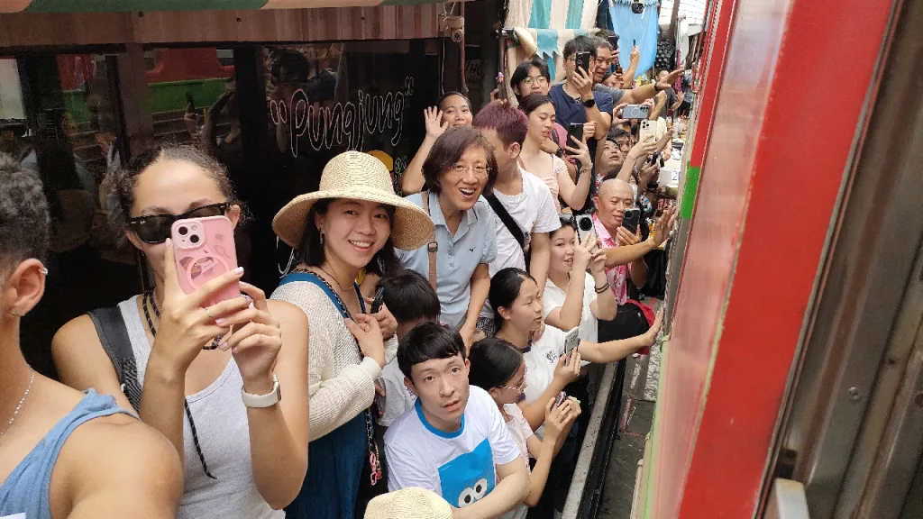 メークロン市場でお店の隙間に立って通過する列車を触る観光客